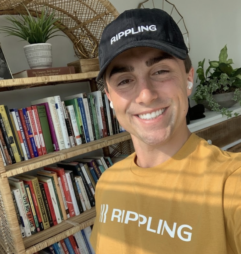 Dalton in a yellow Rippling shirt and hat in front of his bookshelf